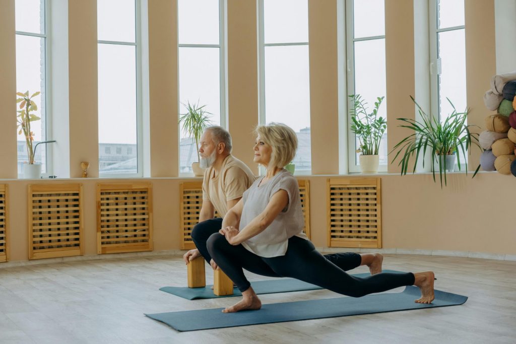Una pareja de ancianos practicando yoga en casa, centrándose en un estilo de vida saludable y la flexibilidad.